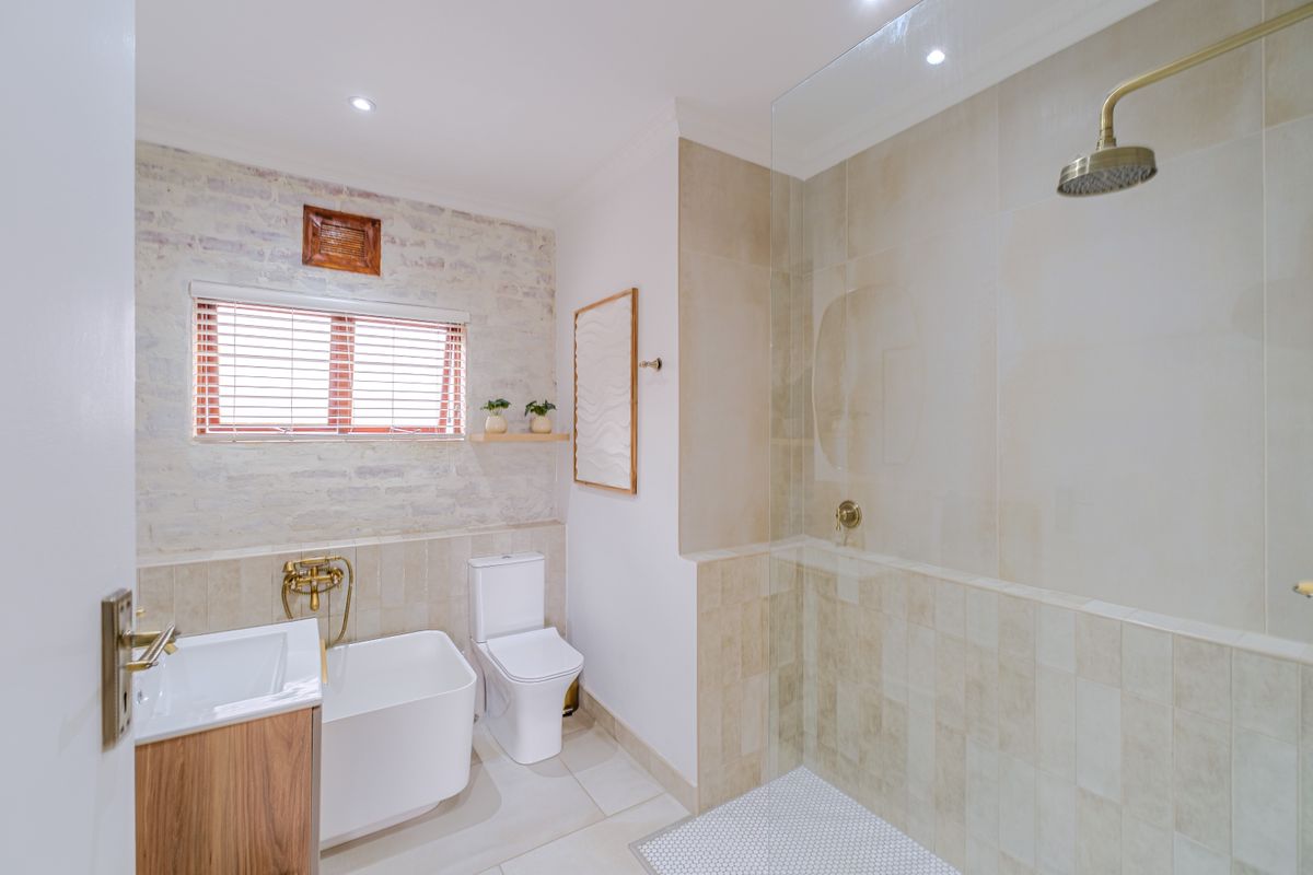 Modern bathroom featuring a spacious walk-in shower with glass screen, wall-mounted toilet, vanity basin, and stylish exposed brick wall detailing.