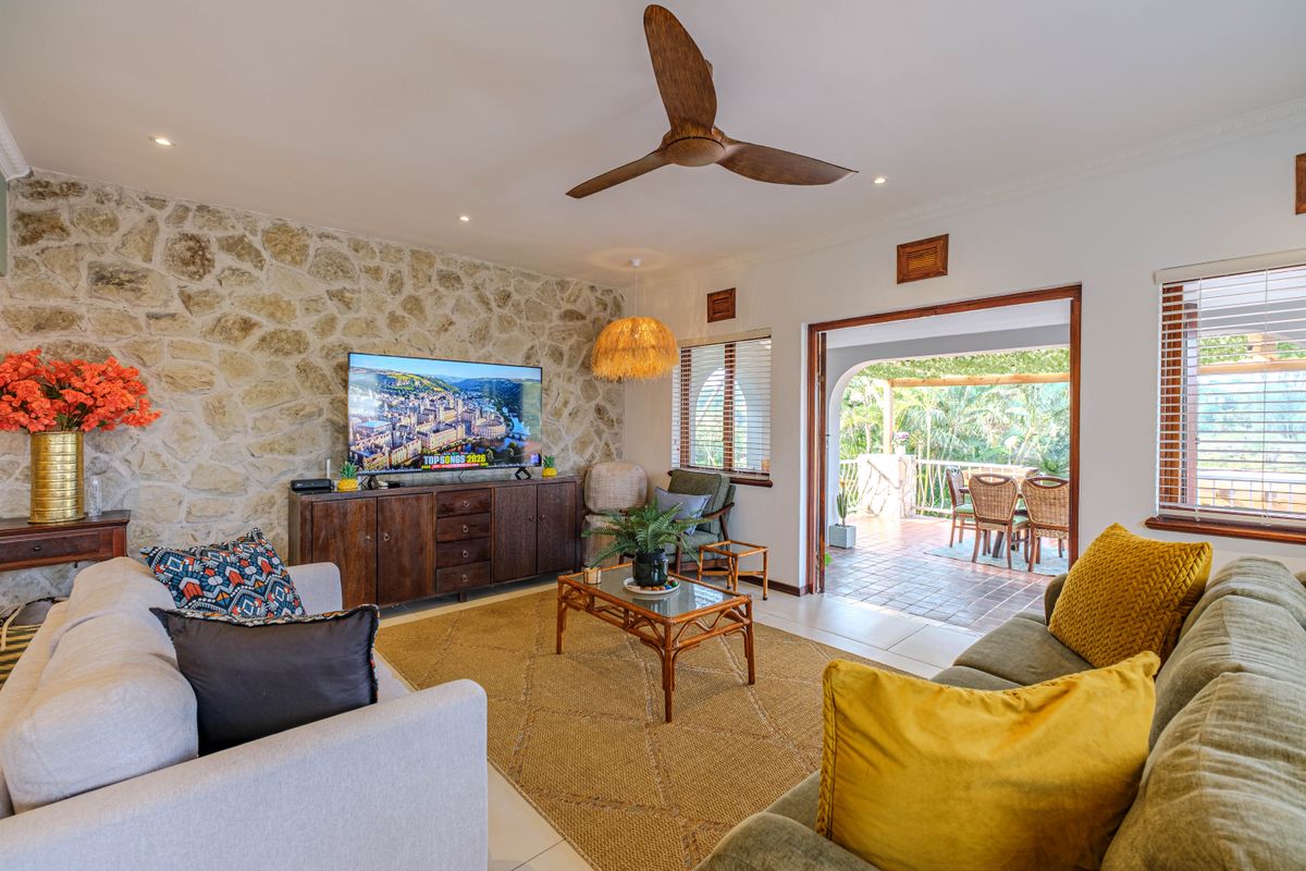 A bright living room featuring a natural stone accent wall, ceiling fan, and direct access to a covered outdoor patio area.