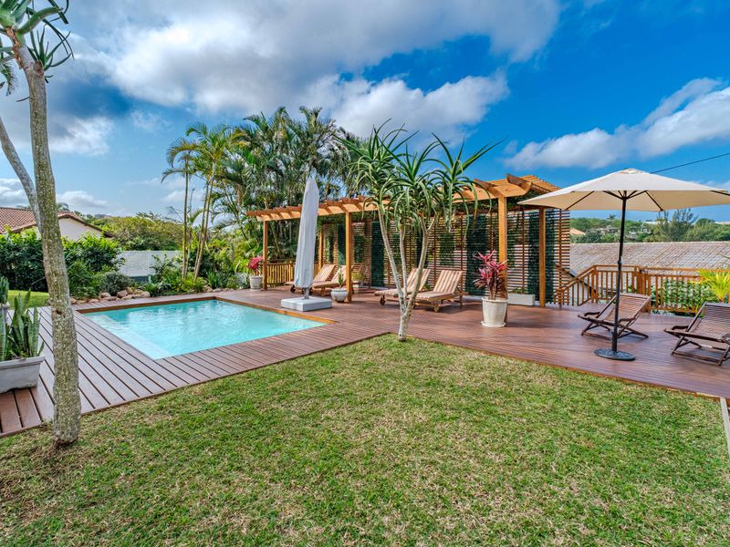 A well-maintained outdoor entertainment area featuring a swimming pool, expansive timber decking, and a wooden pergola, set within a landscaped garden.