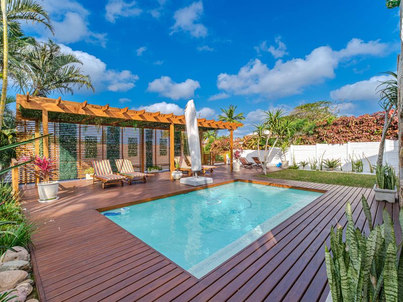 A well-maintained outdoor pool area featuring extensive timber decking, a wooden pergola, and a landscaped garden, perfect for relaxation and outdoor entertainment.