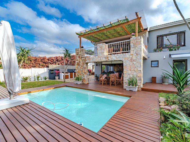 Outdoor entertainment area featuring a swimming pool, timber decking, stone-clad structure with a pergola, and a built-in braai area.