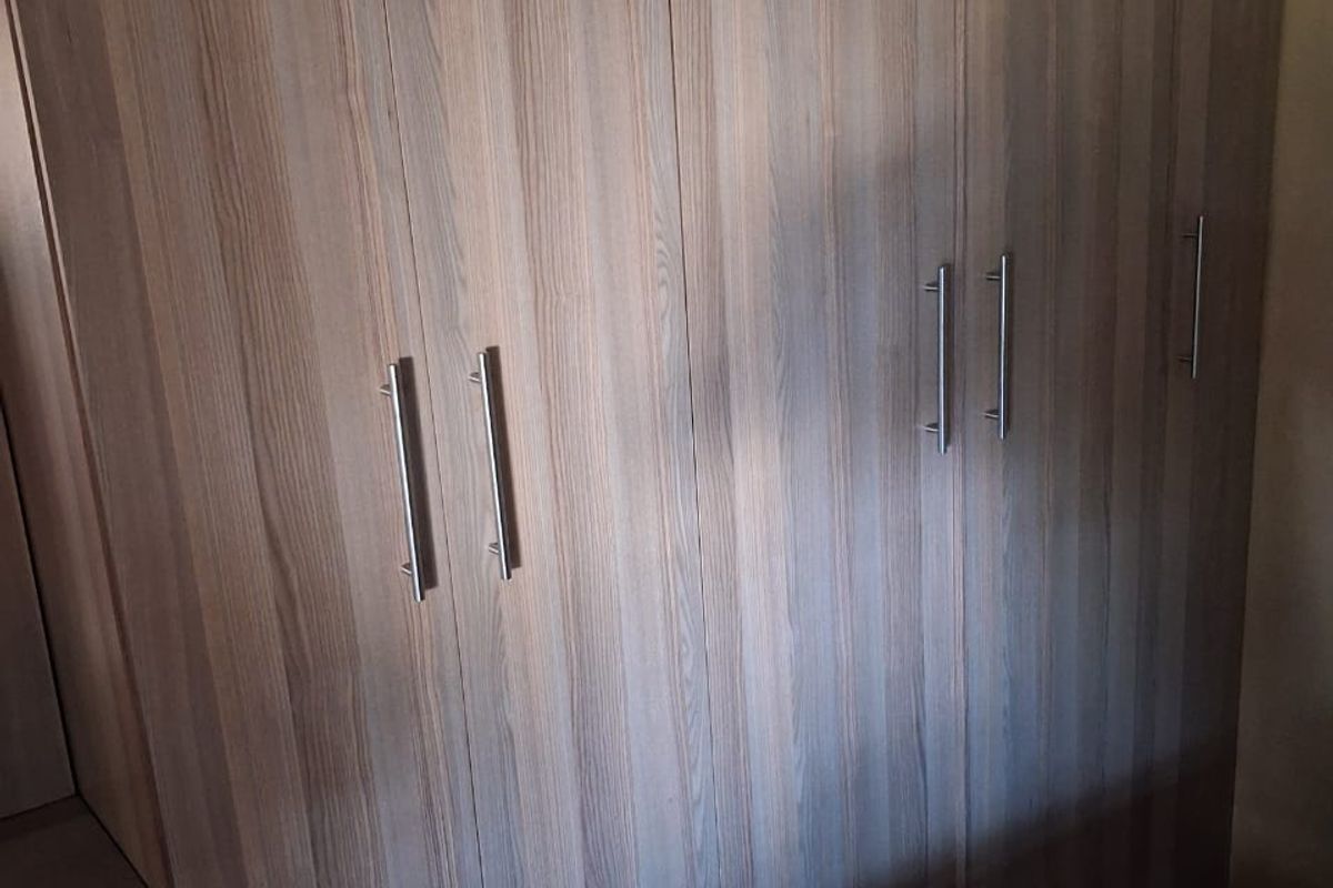 A bedroom featuring floor-to-ceiling built-in wooden cupboards with modern metal handles, providing ample storage space.