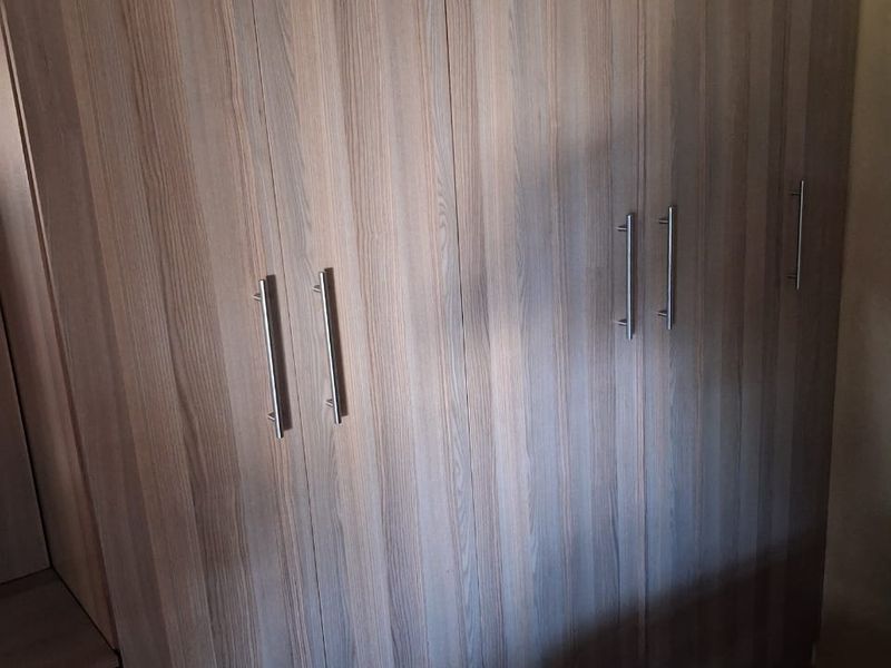 A bedroom featuring floor-to-ceiling built-in wooden cupboards with modern metal handles, providing ample storage space.