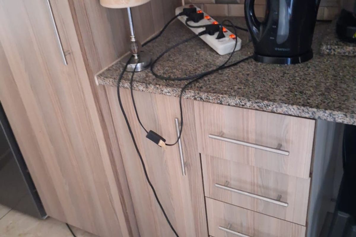 A kitchen corner featuring wood-look laminate cabinetry, granite countertops, and a tiled backsplash, showing a need for improved electrical infrastructure.