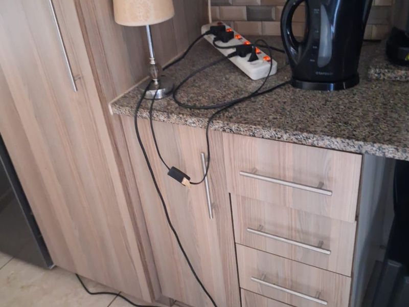A kitchen corner featuring wood-look laminate cabinetry, granite countertops, and a tiled backsplash, showing a need for improved electrical infrastructure.