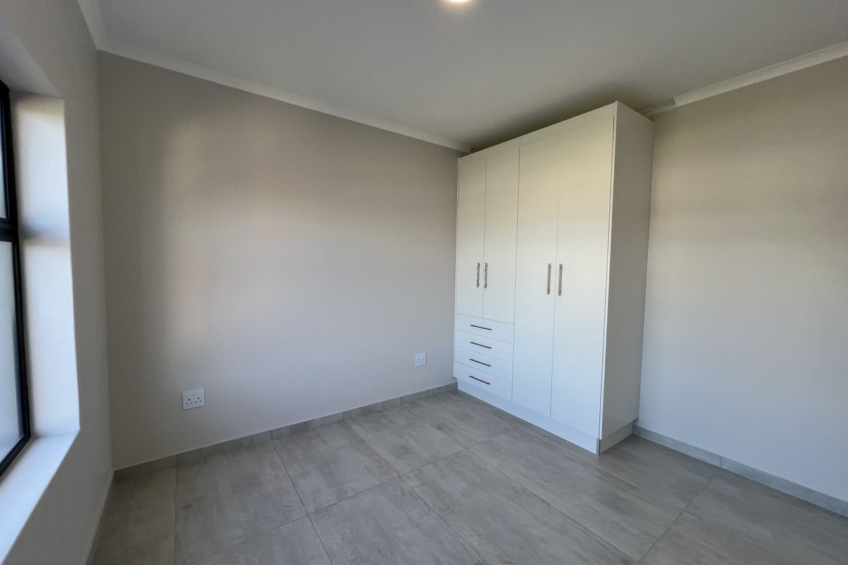 A clean, modern bedroom featuring neutral wall tones, large-format floor tiles, and a spacious white built-in wardrobe.