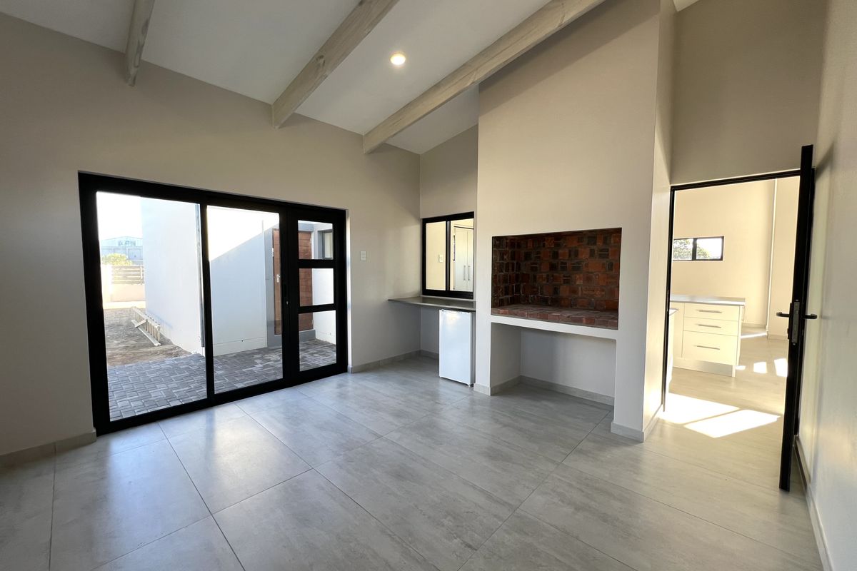 Spacious living area featuring exposed ceiling beams, large sliding doors to the exterior, and a built-in brick braai, offering a modern and bright atmosphere.
