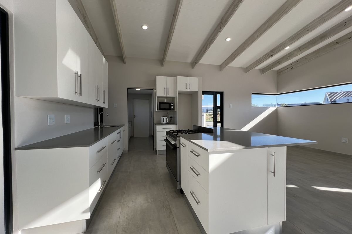 Modern kitchen featuring white cabinetry, stone countertops, a central island, gas stove, and exposed ceiling beams in a bright, open-plan layout.