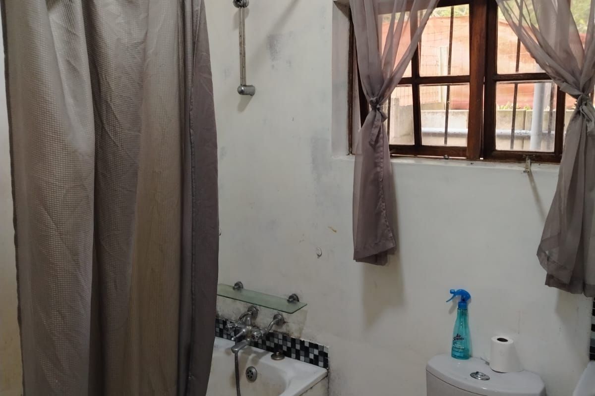A dated bathroom featuring a bathtub with shower mixer, toilet, and timber window frame, requiring significant cosmetic renovation and surface repairs.