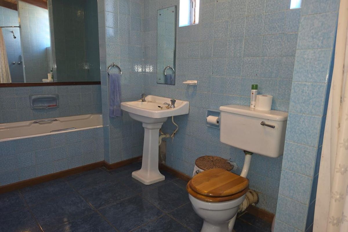 A dated bathroom featuring blue wall and floor tiles, a pedestal basin, and a built-in bathtub.