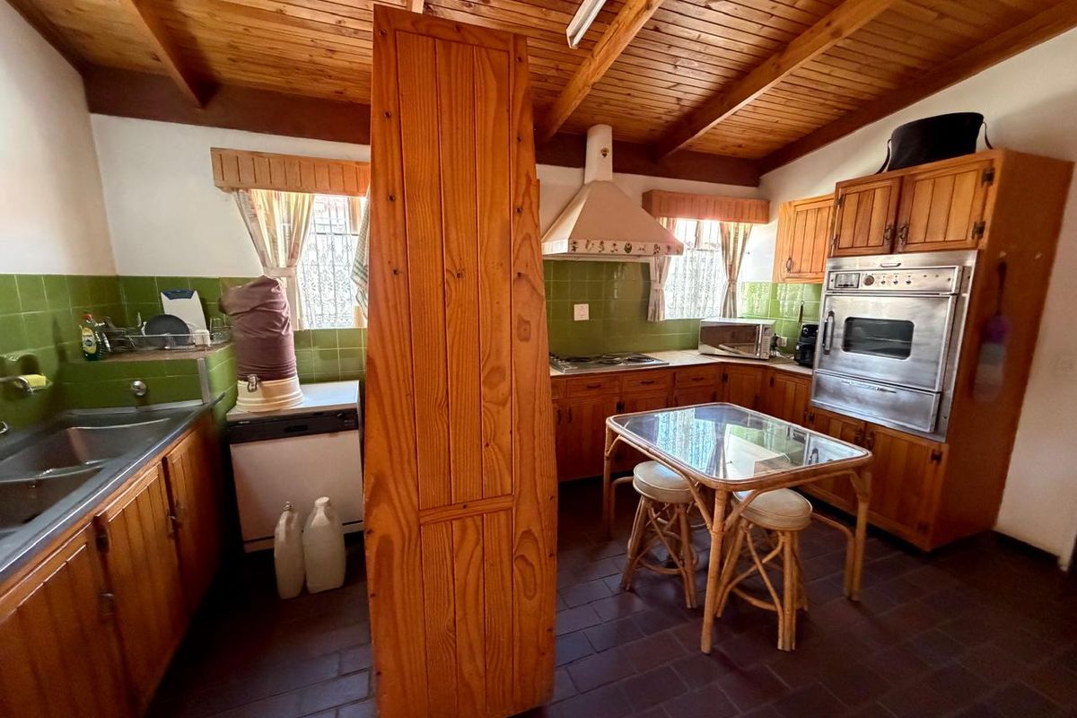 A dated kitchen featuring timber cabinetry, a tiled splashback, built-in oven, and exposed timber ceiling beams.