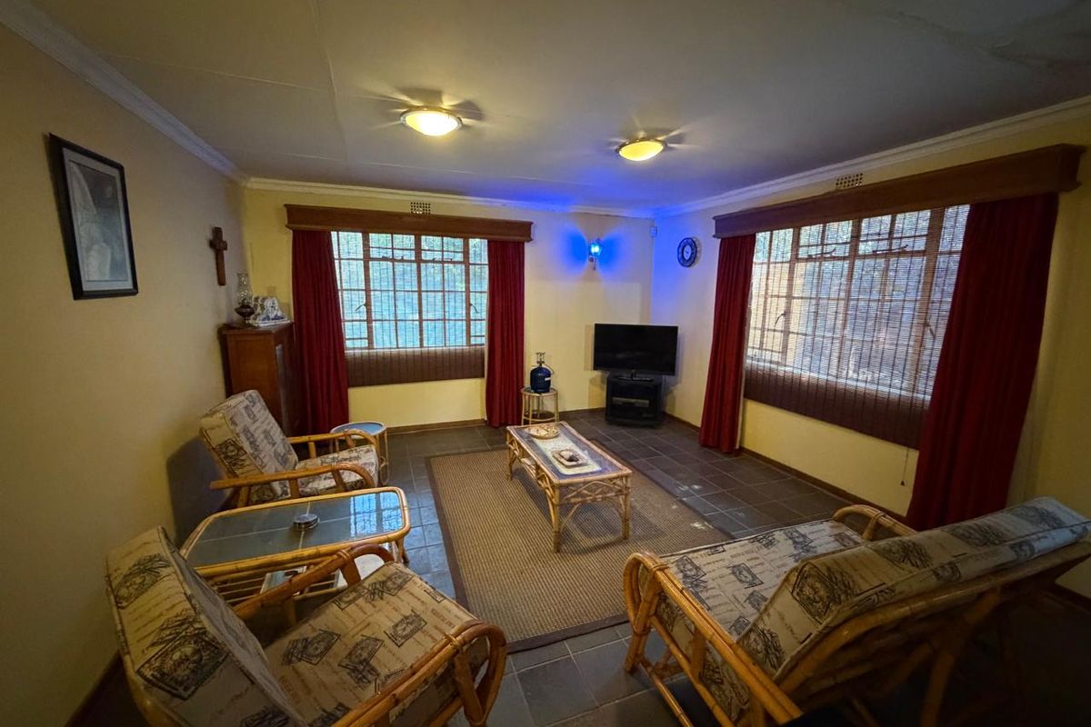 A living room featuring tiled flooring, ceiling lighting, and window security bars, showing signs of ceiling water damage.