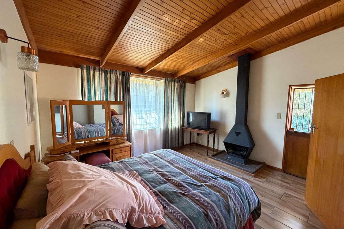 A bedroom featuring a vaulted timber ceiling, tiled flooring, and a prominent freestanding metal fireplace, providing a rustic and cozy atmosphere.