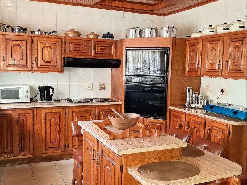A traditional kitchen featuring extensive wooden cabinetry, a central island, built-in oven, and a distinctive wooden ceiling with tiled flooring throughout.