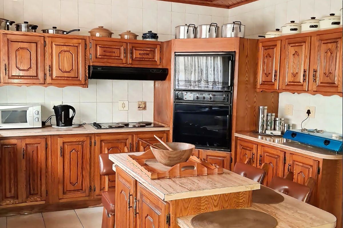 A traditional kitchen featuring extensive wooden cabinetry, a central island, built-in oven, and a distinctive wooden ceiling with tiled flooring throughout.