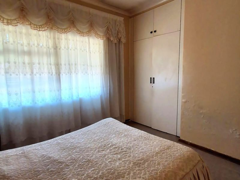Bedroom featuring built-in wardrobe storage, ceiling fan, and carpeted flooring. The room requires cosmetic updates to address wall surface damage and dated finishes.