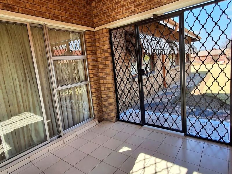 A covered patio area featuring exposed brick walls, a timber ceiling, tiled flooring, and secure sliding glass doors leading to the garden.