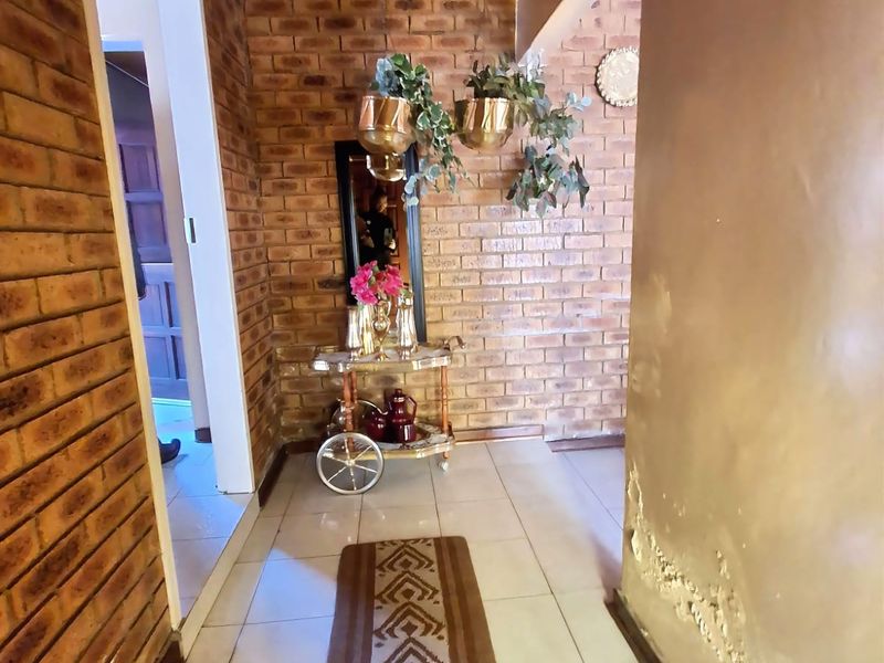 A hallway featuring exposed brick walls, timber ceiling, and tiled flooring, showing signs of damp and paint deterioration on the plaster wall.