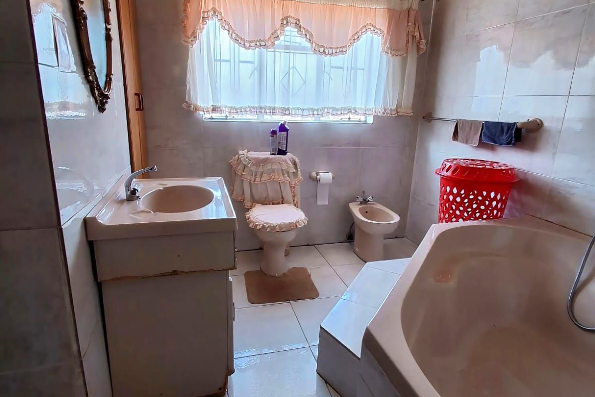 A dated bathroom featuring a corner bathtub, vanity basin, toilet, and bidet with full-height wall tiling.