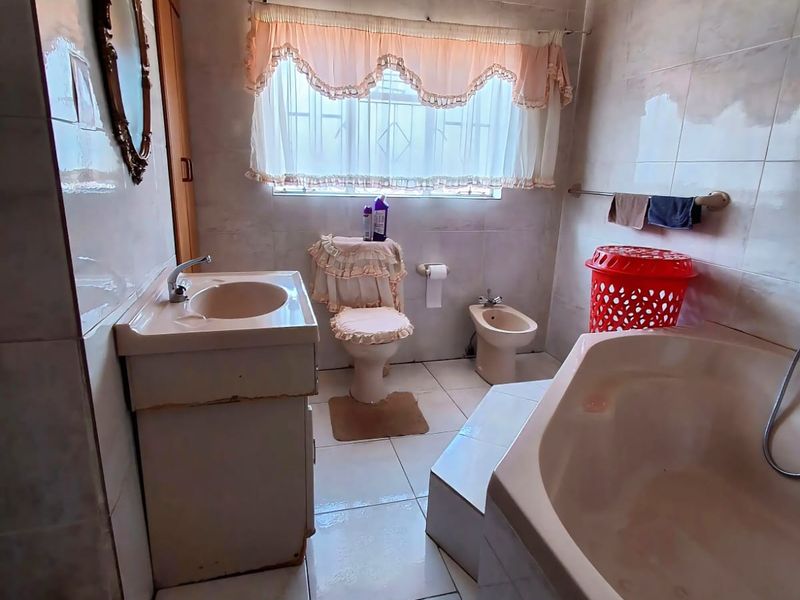 A dated bathroom featuring a corner bathtub, vanity basin, toilet, and bidet with full-height wall tiling.