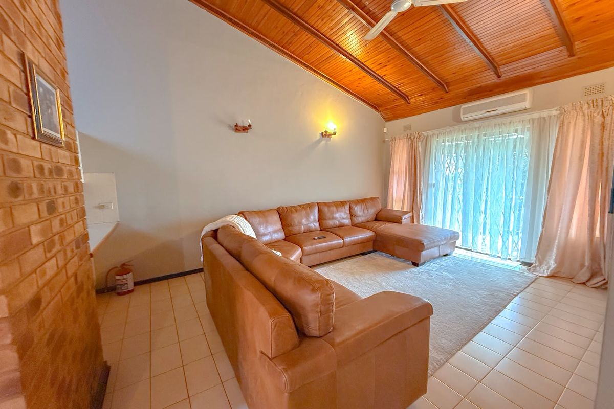 Spacious living room featuring a high exposed timber raked ceiling, tiled flooring, split system air conditioning, and direct access to the outdoor area.