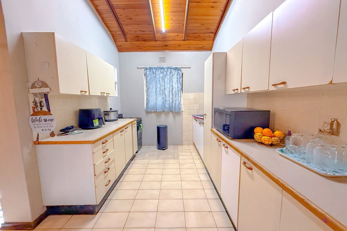 A galley-style kitchen featuring tiled flooring, timber ceiling, and ample laminate cabinetry with a tiled splashback.