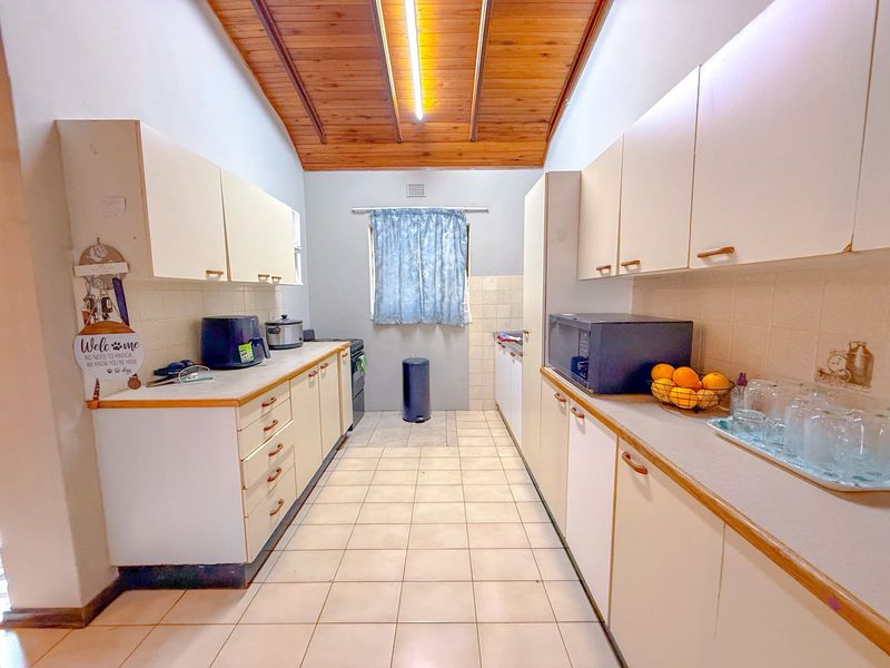 A galley-style kitchen featuring tiled flooring, timber ceiling, and ample laminate cabinetry with a tiled splashback.