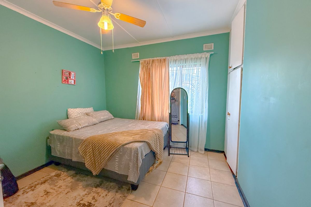 A bedroom featuring tiled flooring, a ceiling fan, and built-in cupboards, offering a functional space with potential for cosmetic updates.