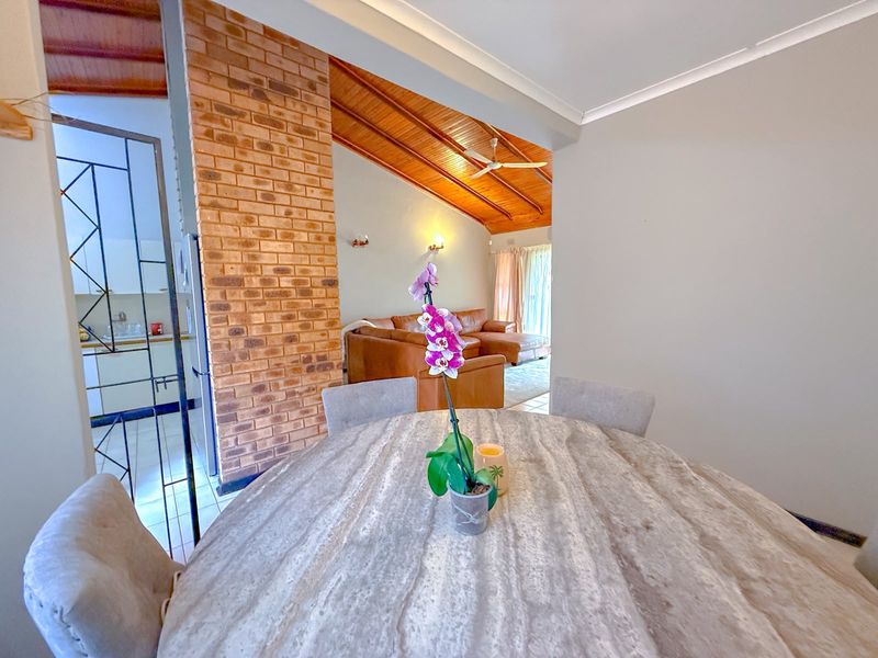 Open plan living and dining area featuring a striking exposed brick wall, vaulted timber ceilings, and tiled flooring, creating a warm and inviting atmosphere.