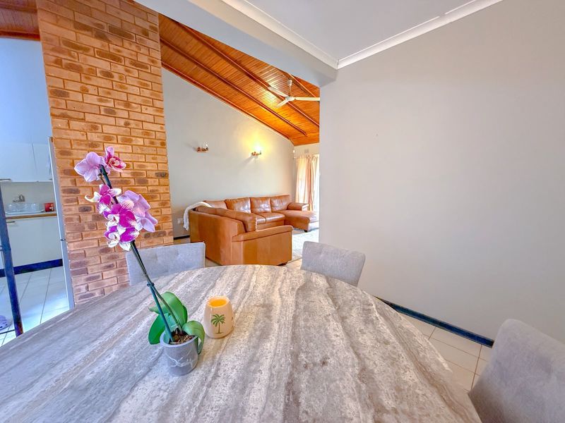 Spacious open-plan living and dining area featuring a striking exposed brick pillar, vaulted timber ceilings, and neutral tiled flooring.