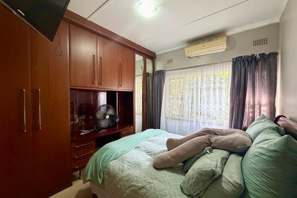 A bedroom featuring extensive built-in wooden cabinetry, a wall-mounted air conditioning unit, and a window fitted with a security gate.