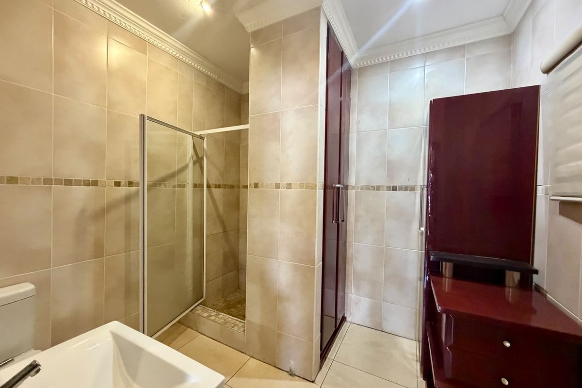 A functional bathroom featuring a glass-enclosed shower, neutral wall tiling, and built-in cabinetry with a glossy finish.