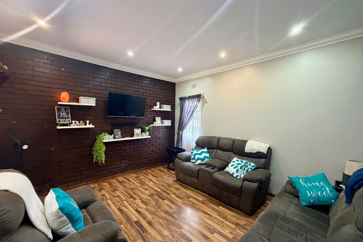 A comfortable living room featuring a dark exposed brick feature wall, recessed downlighting, and modern laminate timber flooring.