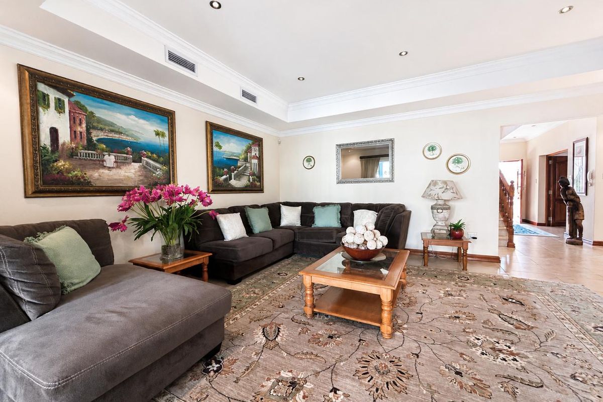 Spacious living room featuring a recessed ceiling with downlights, ducted air conditioning, crown molding, and neutral tiled flooring.