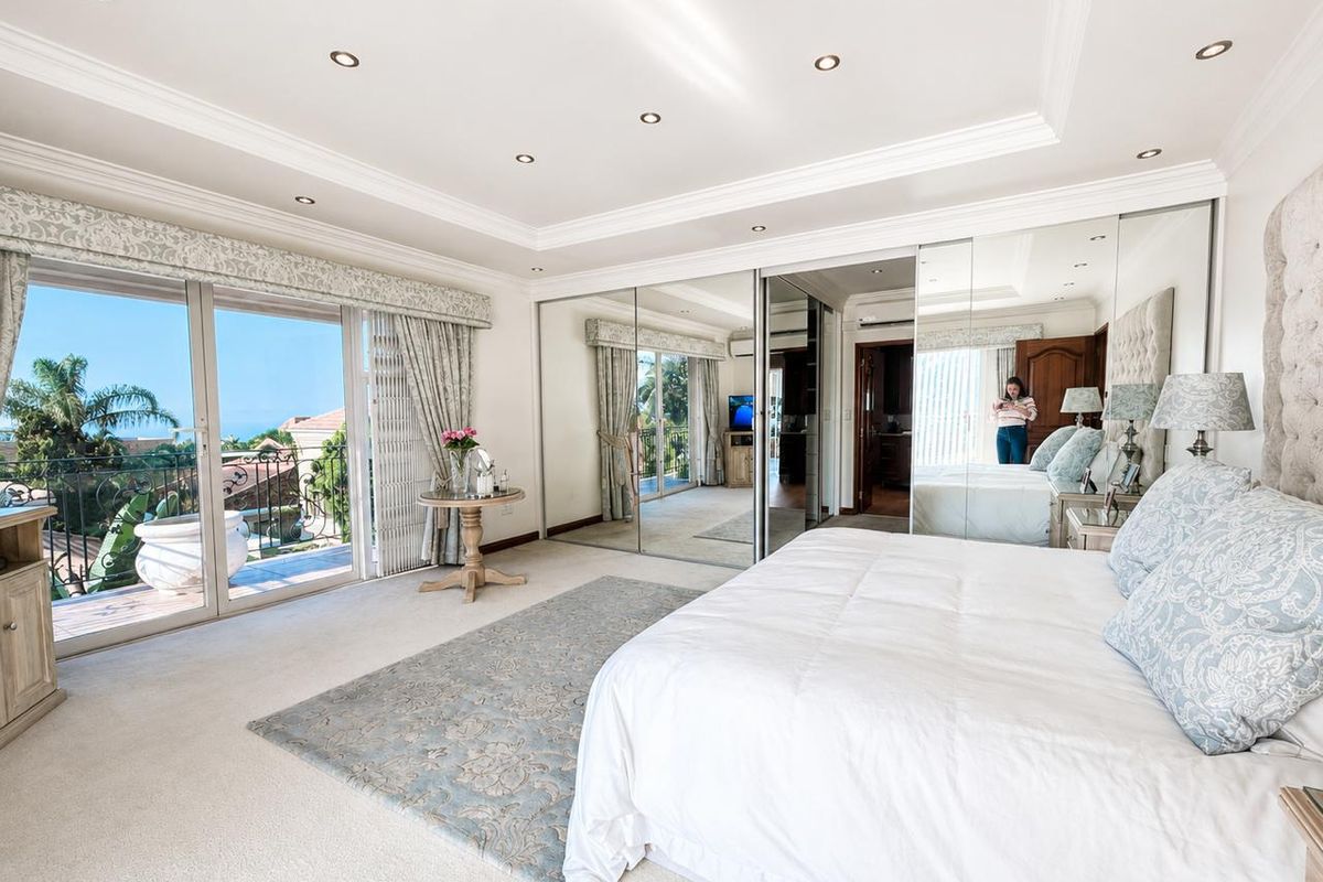 Spacious bedroom featuring large mirrored built-in wardrobes, recessed ceiling lighting, and sliding glass doors opening onto a private balcony with scenic views.