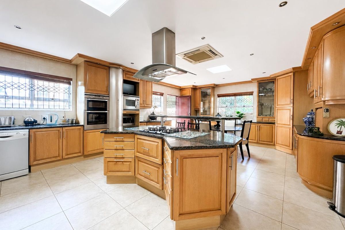Spacious kitchen featuring a large central island with gas hob, granite countertops, built-in double ovens, ample wooden cabinetry, and natural light from overhead skylights.