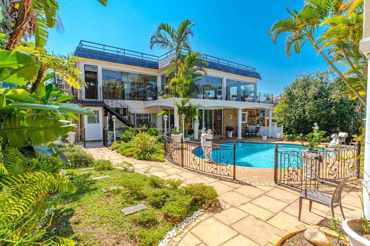 Rear view of the property featuring a swimming pool, paved patio area, and a spacious upper-level balcony with glass enclosures.