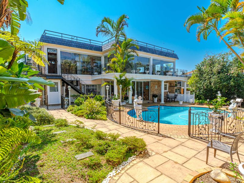 Rear view of the property featuring a swimming pool, paved patio area, and a spacious upper-level balcony with glass enclosures.