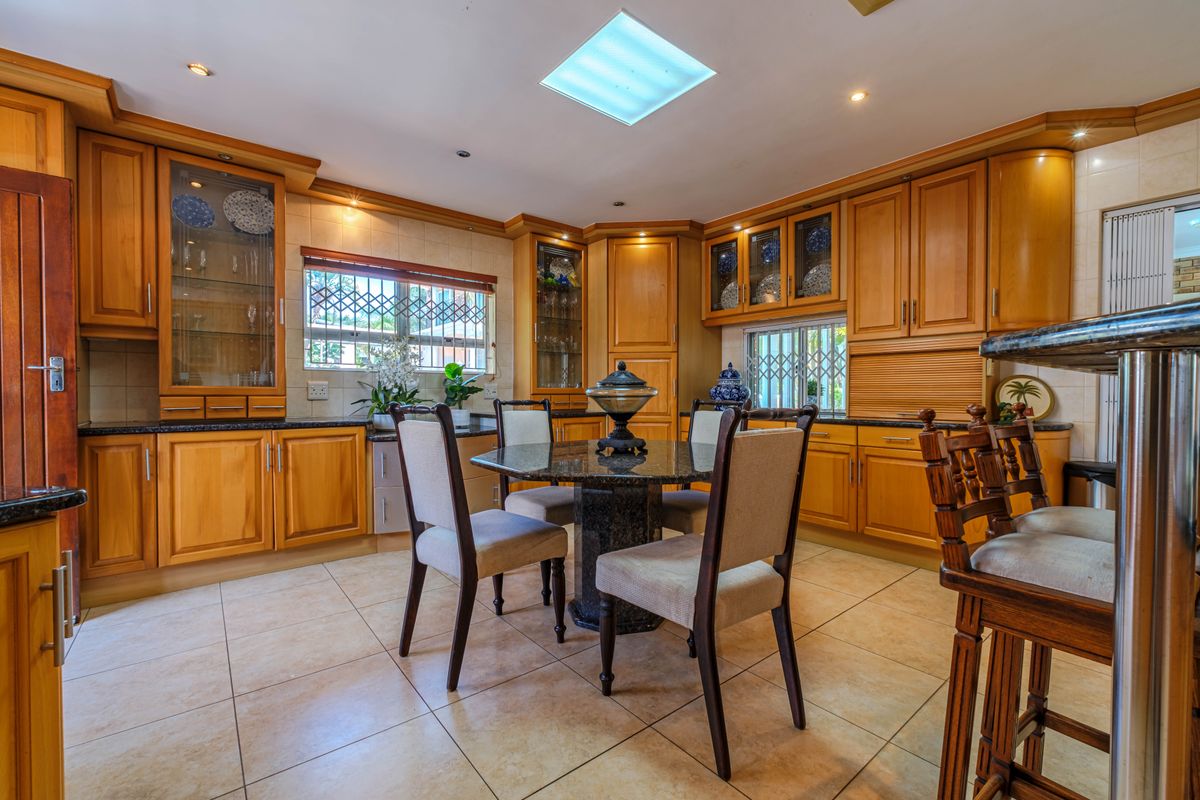 A spacious kitchen featuring warm wooden cabinetry, granite countertops, tiled flooring, and a central skylight, providing a functional and traditional cooking and dining space.