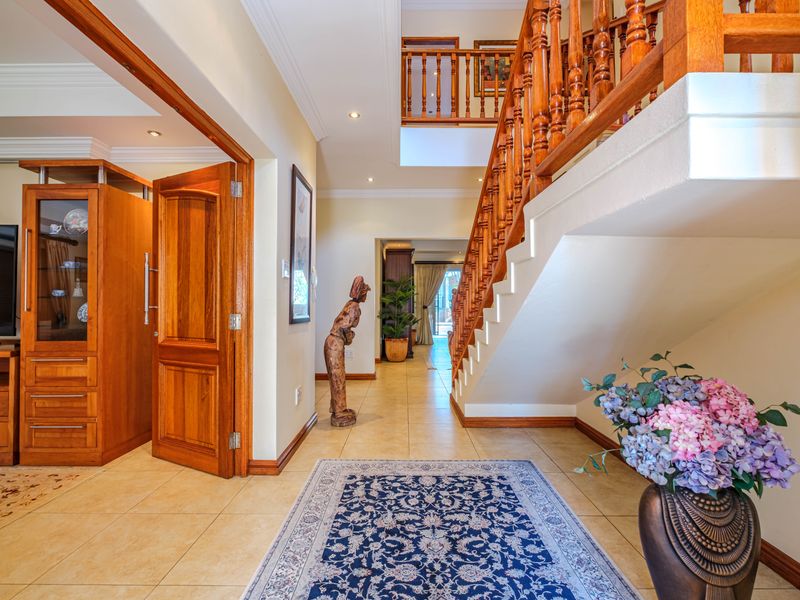 Spacious entrance hall featuring a grand wooden staircase with balustrade, tiled flooring, and recessed lighting, leading into the main living areas.