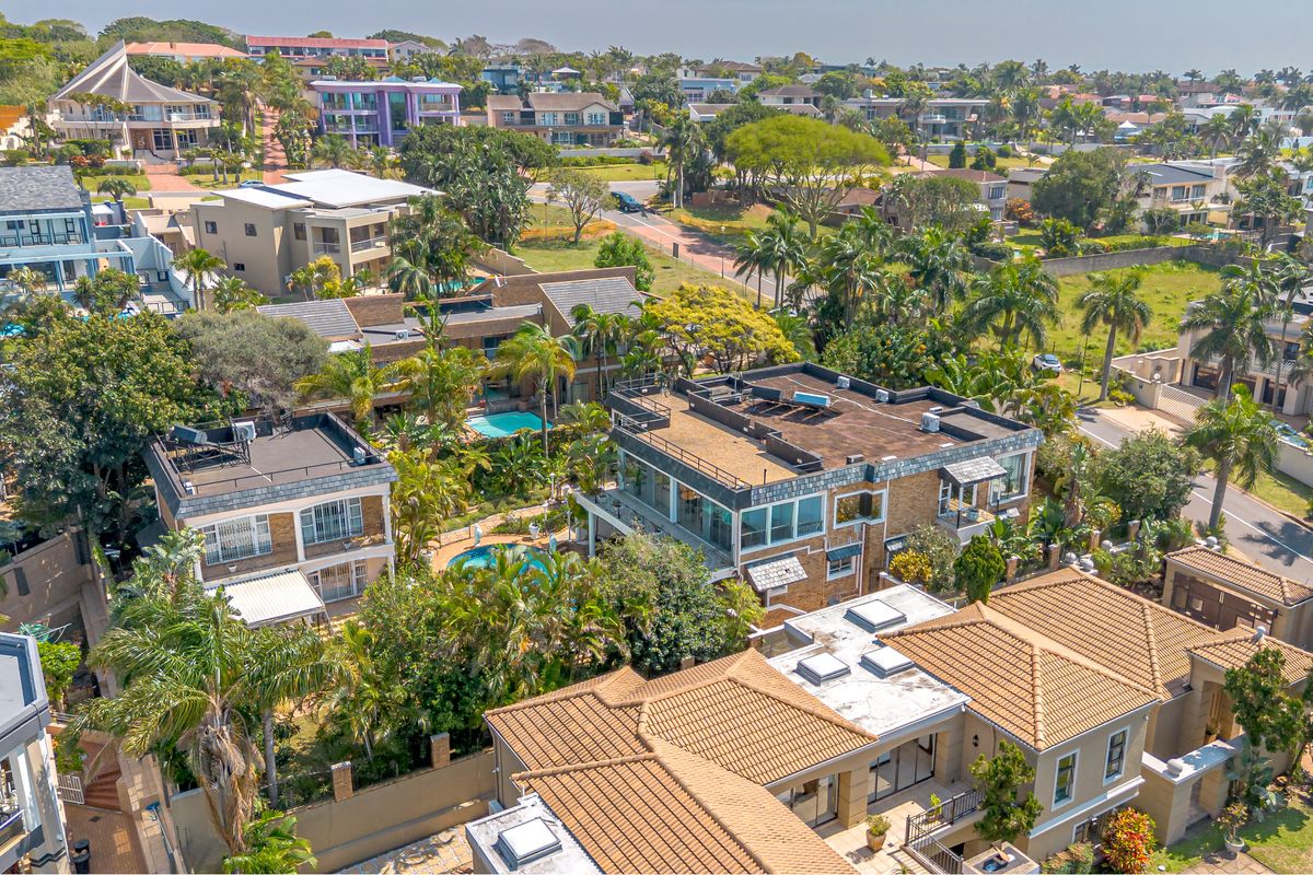 An elevated aerial view of a residential estate featuring multiple homes with swimming pools, landscaped gardens, and various roof styles.