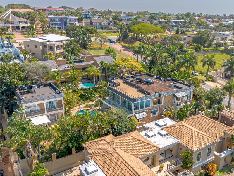 An elevated aerial view of a residential estate featuring multiple homes with swimming pools, landscaped gardens, and various roof styles.