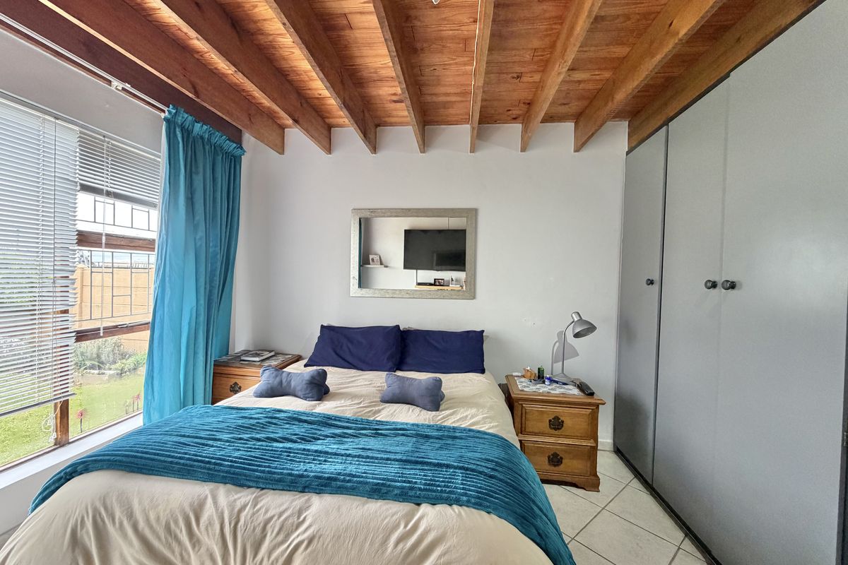 A bedroom featuring exposed timber ceiling beams, tiled flooring, and built-in cupboards, offering a functional space with natural light.