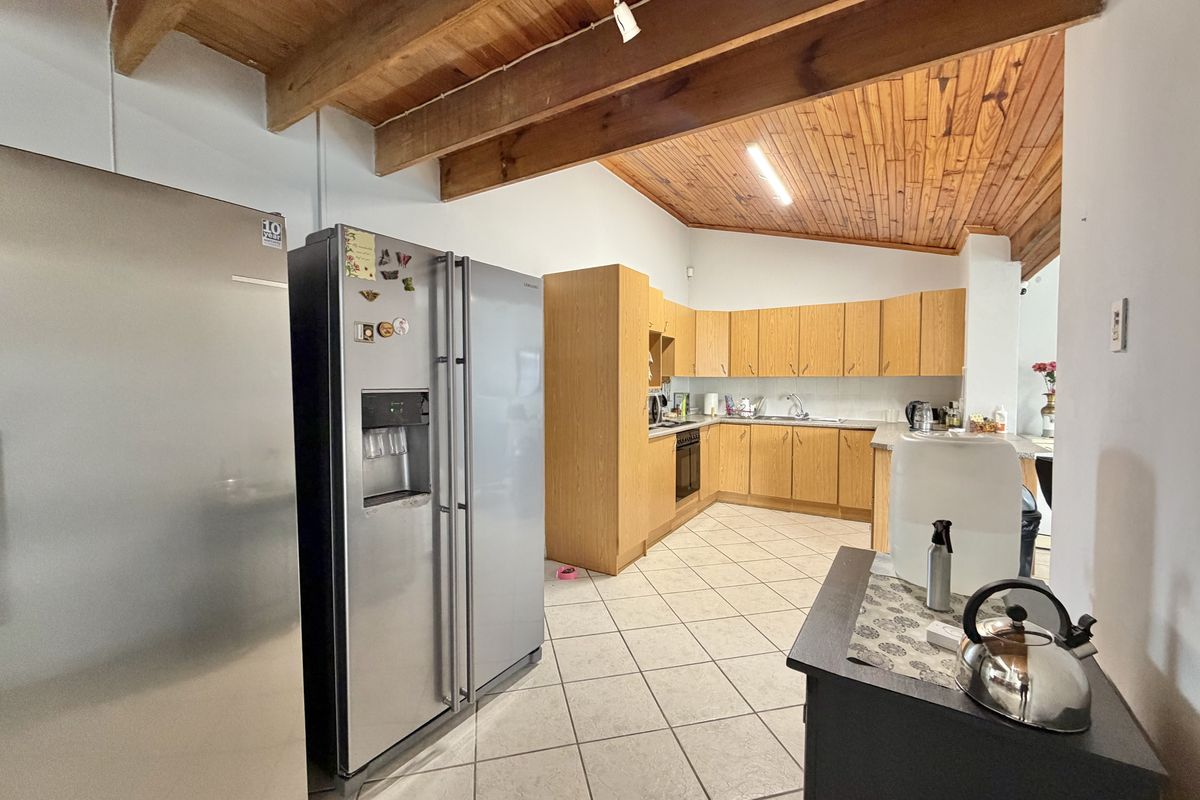 Spacious kitchen featuring timber ceiling beams, wooden cabinetry, tiled flooring, and a functional layout with built-in appliances.