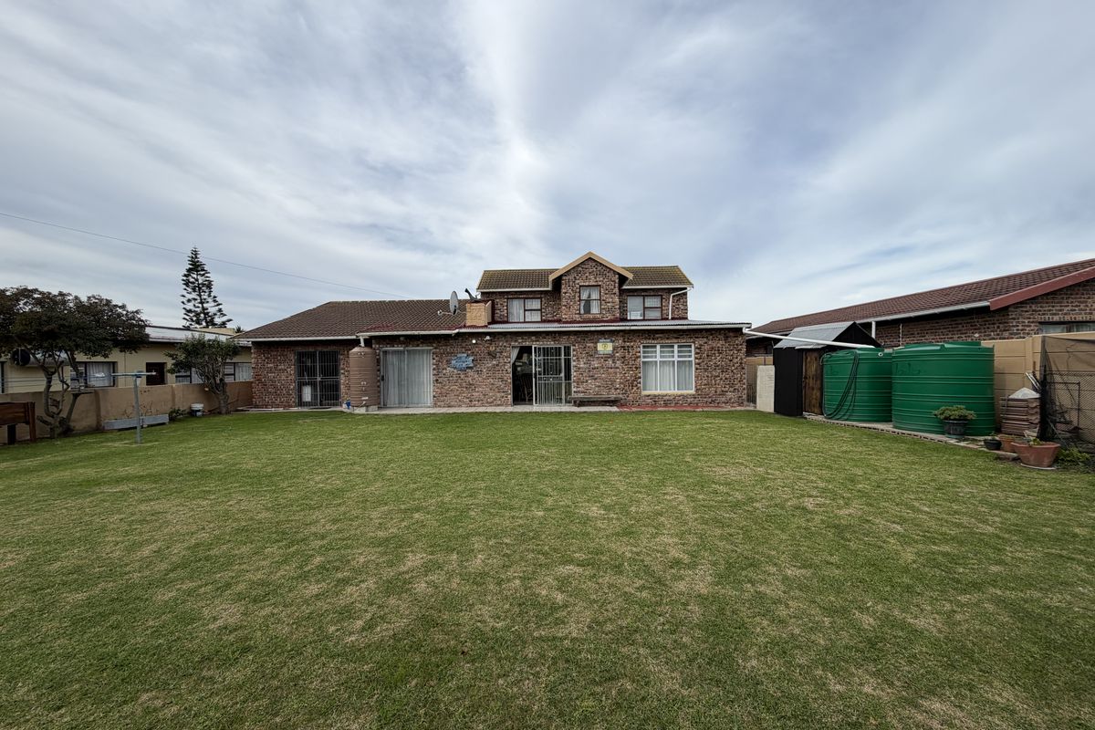 Rear view of a double-story brick house featuring a large lawn, sliding door access, and external water storage tanks.