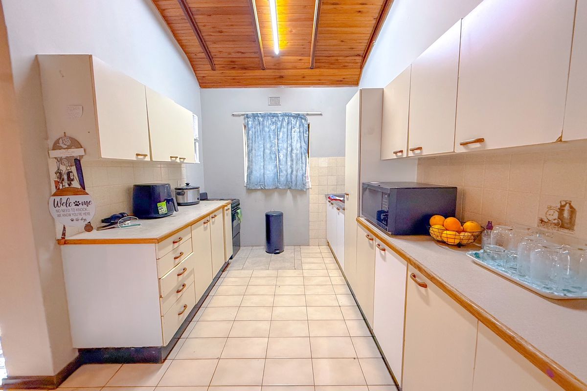 A functional galley-style kitchen featuring tiled flooring, ample laminate cabinetry, a tiled backsplash, and a distinctive timber-paneled ceiling.