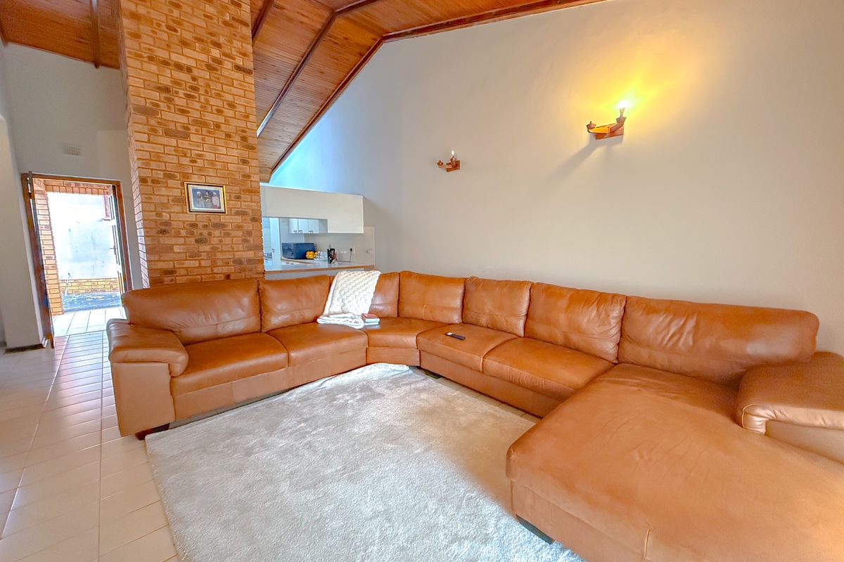 Spacious living room featuring a vaulted timber ceiling, exposed brick fireplace, and tiled flooring, with direct access to an outdoor area.