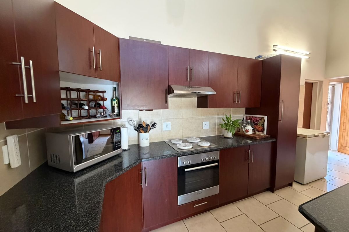 A functional kitchen featuring dark wood cabinetry, granite countertops, a built-in oven, and an electric hob with an extractor fan.