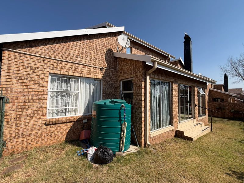 Rear view of the townhouse featuring face brick exterior, sliding glass doors, a chimney, and an installed water storage tank in the garden area.