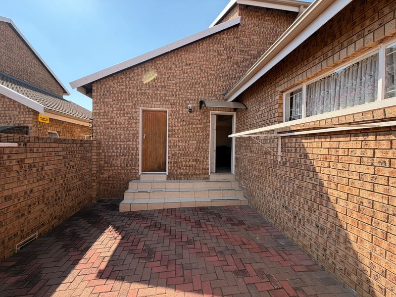 A private rear courtyard featuring face brick walls, paved flooring, and tiled steps leading to the rear entrance of the townhouse.
